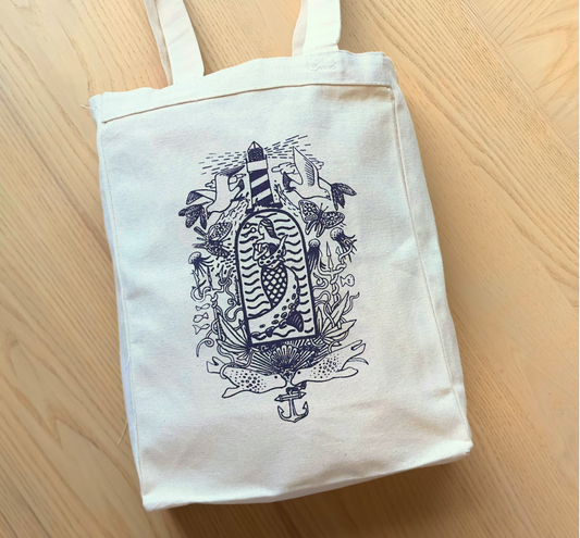 The SeaWeed Co. Canvas Tote - Purple is perfect for Maine adventures, featuring an illustrated lighthouse, waves, and sea creatures on cream-colored canvas. Resting on a light wooden floor, it beautifully captures a nautical theme.