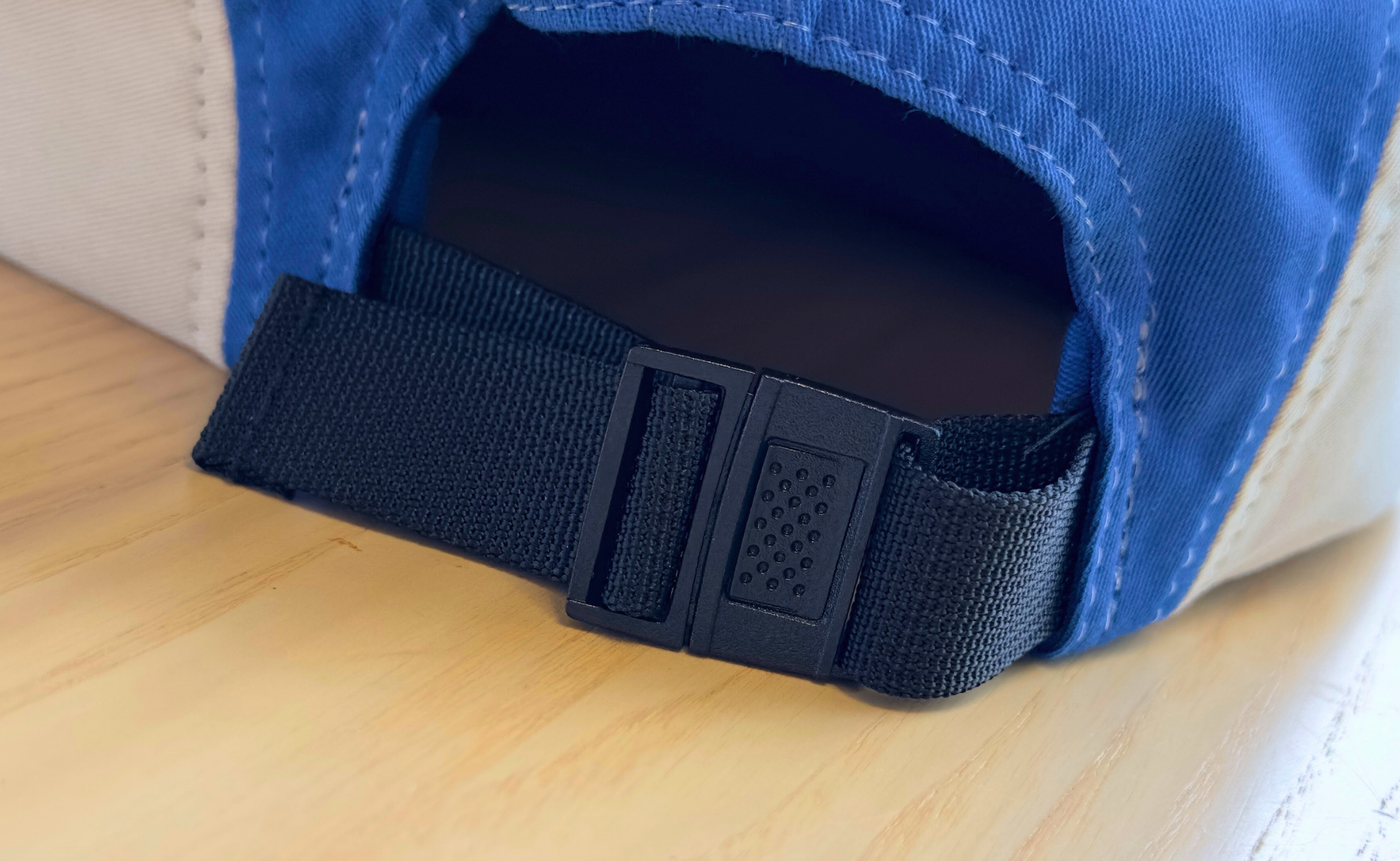 Close-up of SeaWeed Co.s Colorblock Hat in blue and beige, featuring an adjustable black strap and signature buckle, resting on a wooden surface.