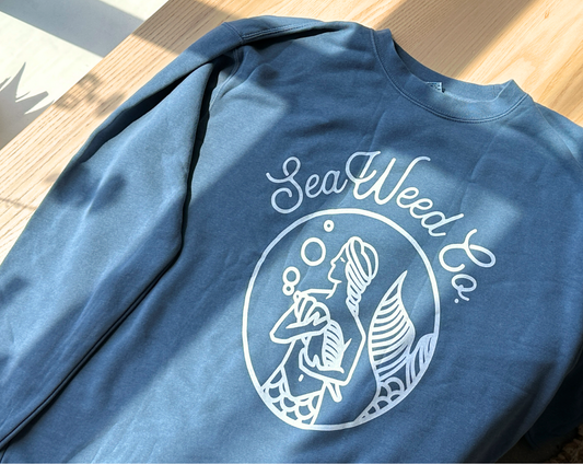 A slate-colored crewneck sweatshirt with a graphic of a mermaid and the text 'SeaWeed Co.'