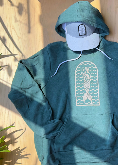 A forest green hoodie with a beige mermaid arch logo on the front and 'Seaweed Co.' script on the back.